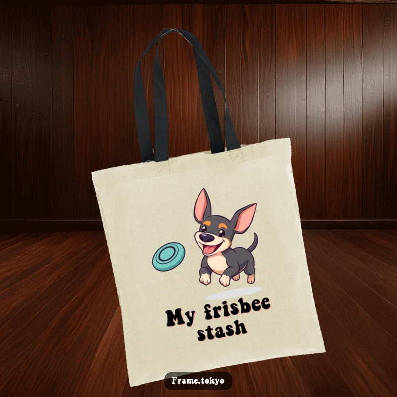 Funny pinscher tote bag showing a dog with a goofy grin playfully chasing a bouncing mini frisbee, ideal for outdoor fun.
